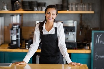 Portrait of smiling waitress standing at counter - obrazy, fototapety, plakaty