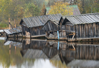 Old dilapidated barns for boats reflected in river.
