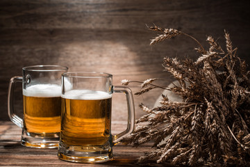 Two mugs of beer with wheat spikelets on wooden background