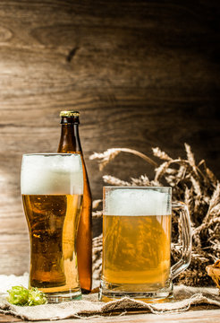 Mug, glasse, bottle of beer with foam on blank wooden background