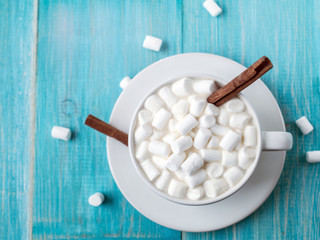A cup of hot cocoa with marshmallows and sticks of cinnamon on a bright blue wooden background shabby. Shallow Selective focus. Top view.