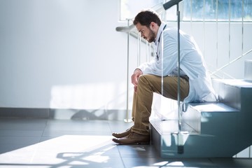 Sad doctor sitting on staircase in hospital