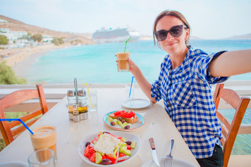 Young woman having lunch with delicious fresh greek salad, frappe and brusketa served for lunch at...