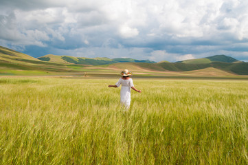 Fototapeta premium Girl in White dress and straw hat walking among fields in countryside 