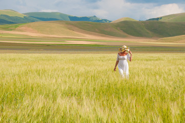 Fototapeta premium Girl in White dress and straw hat walking among fields in countryside