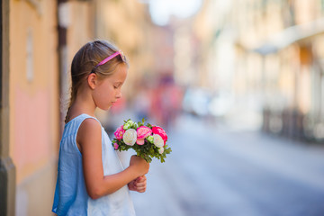 Adorable little girl with flowers bouquet walking in european city