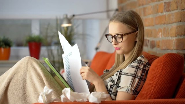 Woman having runny nose and feeling sick while working on papers
