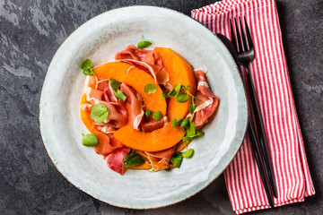 Ham jamon, melon and arugula salad on grey plate