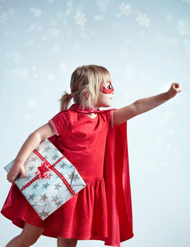 Super gifts for super kids or Special delivery for Christmas. Little girl wearing a superhero costume and a mask posing as a superhero and holding a big gift box