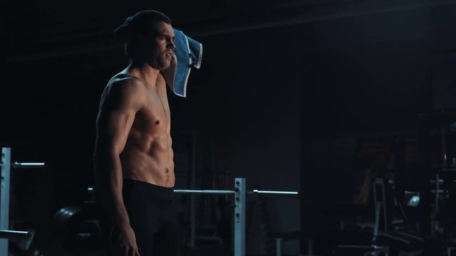 Strong toned young athlete towelling off in a gym wiping away sweat after doing a strenuous workout showing off his muscular physique, with copy space
