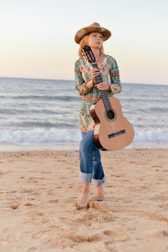 Portrait of a beautiful blond female playing guitar on the beach, sunset sunny blue sky outdoors background