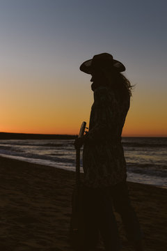 Silhouette of a beautiful female playing guitar on the beach, sunset sunny blue sky outdoors background