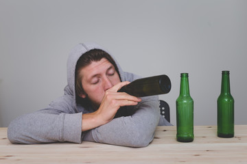 young tired depressed man sitting with beer bottles in empty room indoors