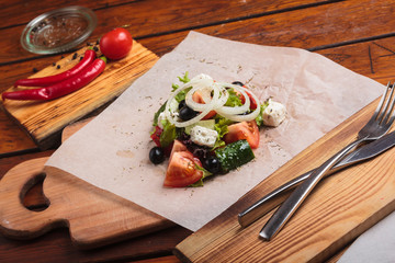 Concept: restaurant menus, healthy eating, homemade, gourmands, gluttony. Greek salad served on paper with ingredients on weathered wooden background.