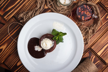 Concept: restaurant menus, healthy eating, homemade, gourmands, gluttony. White plate with chocolate fondant and ice cream on a messy vintage wooden background. Top-down view.