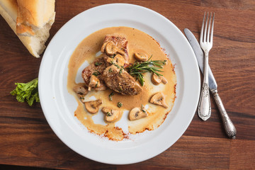 Concept: restaurant menus, healthy eating, homemade, gourmands, gluttony. White plate of pork medallions with mushroom sauce on weathered wooden table. Top-down view