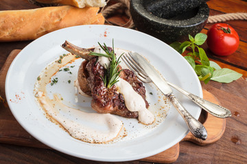 Concept: restaurant menus, healthy eating, homemade, gourmands, gluttony. White plate of lamb rack on wooden table and ingredients on background.