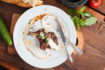 Concept: restaurant menus, healthy eating, homemade, gourmands, gluttony. White plate of lamb rack on wooden table and ingredients on background. Top-down view