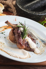 Concept: restaurant menus, healthy eating, homemade, gourmands, gluttony. White plate of lamb rack on wooden table and ingredients on background.