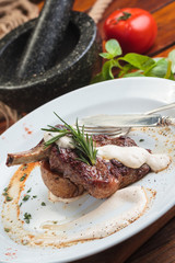 Concept: restaurant menus, healthy eating, homemade, gourmands, gluttony. White plate of lamb rack on wooden table and ingredients on background.