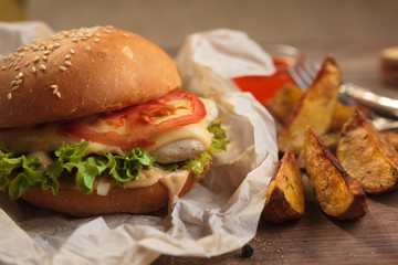 Concept: restaurant menus, healthy eating, homemade, gourmands, gluttony. Classic burger with chicken with ingredients and potato wedges on messy vintage wooden background.