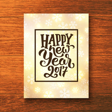 Happy New Year 2017 lettering text in frame on glowing winter background. Vector greeting card template with typography for holidays above wooden backdrop.