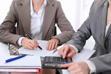 Two female accountants counting on calculator income for tax form completion hands closeup. Internal Revenue Service inspector checking financial document. Planning budget, audit  concept