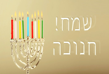 Menorah with candles for Hanukkah on color background. Hanukkah celebration concept. Text HAPPY HANUKKAH in Hebrew