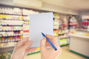 Woman with notebook in store, closeup. Blank paper.