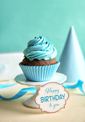 Delicious cupcake and greeting card on table. Text HAPPY BIRTHDAY TO YOU on card.
