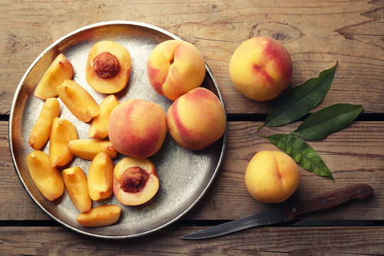 Fresh juicy peaches in silver tray and knife on wooden background