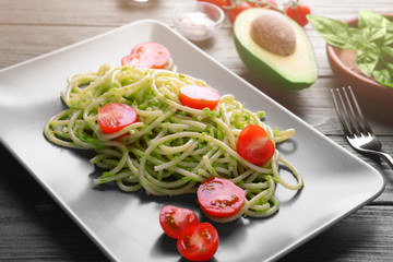 Spaghetti with cherry tomatoes and avocado sauce on wooden table closeup