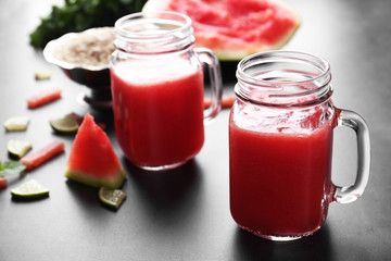 Jugs with smoothie, watermelon and lime slices and mint on grey table