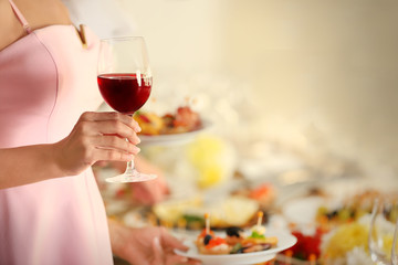 Woman holding glass of red wine on blurred background, close up view