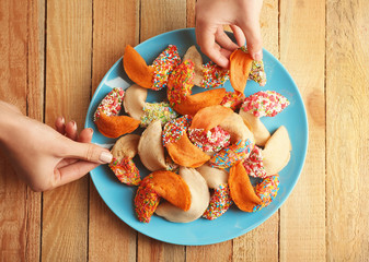 Hands taking colorful fortune cookies from plate on wooden background