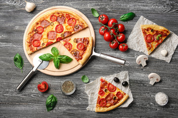 Delicious pizza with slices and ingredients on table