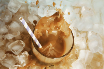 Glass of cold coffee with ice cubes and splashes on table