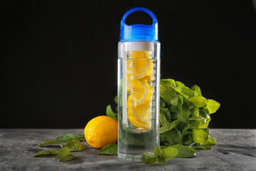 Water with lemon in bottle and fresh fruits on black background