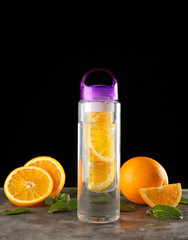 Water with oranges in bottle and fresh fruits on black background