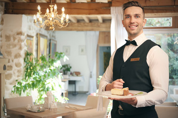 Handsome young waiter serving dessert at restaurant