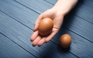 Female hand with egg on wooden background, closeup