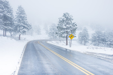 Beautiful winter scene with icy slick road driving situation curving road covered with snow and snowy trees all around
