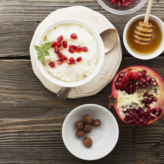 Fragrant warm homemade rice milk porridge with sugar and pomegranate seeds on a wooden background. The concept of healthy, seasonal dishes