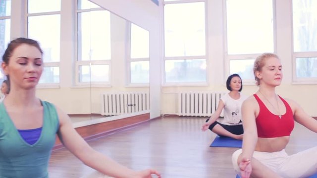 Young girls and fitness, sport, training, yoga. Group yoga concept. Yoga team in gym class in lotus or baddha Konasana or butterfly pose, posture, slow motion 50 fps.