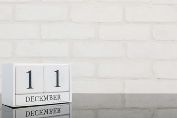 Fototapeta na wymiar Closeup white wooden calendar with black 11 december word on black glass table and white brick wall textured background with copy space , selective focus at the calendar