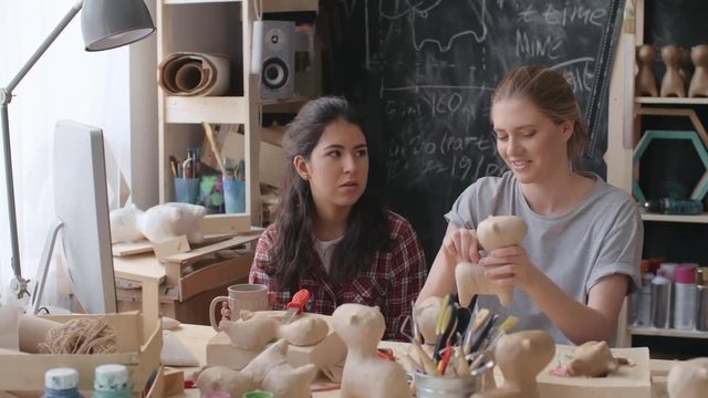 PAN of young woman sitting in workshop drinking tea and chatting with her colleague working on binding two pieces of papier-mache figure together 