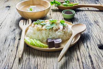 Hainanese chicken rice  in a plate along with the Soup and sauce on a wooden table. Hainanese chicken rice is popular in Asia.