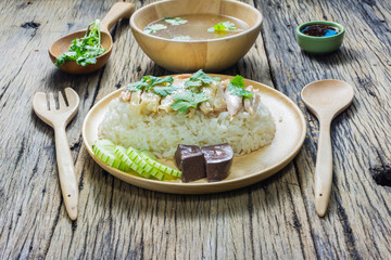 Hainanese chicken rice  in a plate along with the Soup and sauce on a wooden table. Hainanese chicken rice is popular in Asia.