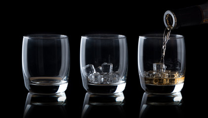 Pouring whiskey into glass  isolated on black background