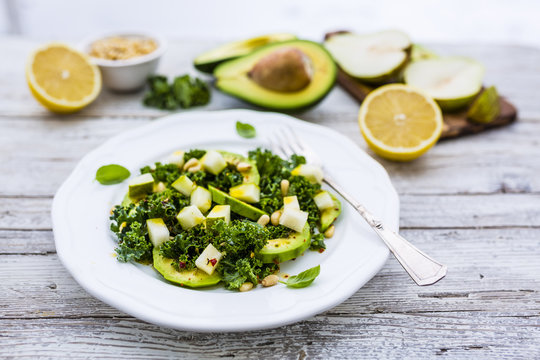 Fresh salad with kale leaves and avocado with pear on a white plate on wooden table.